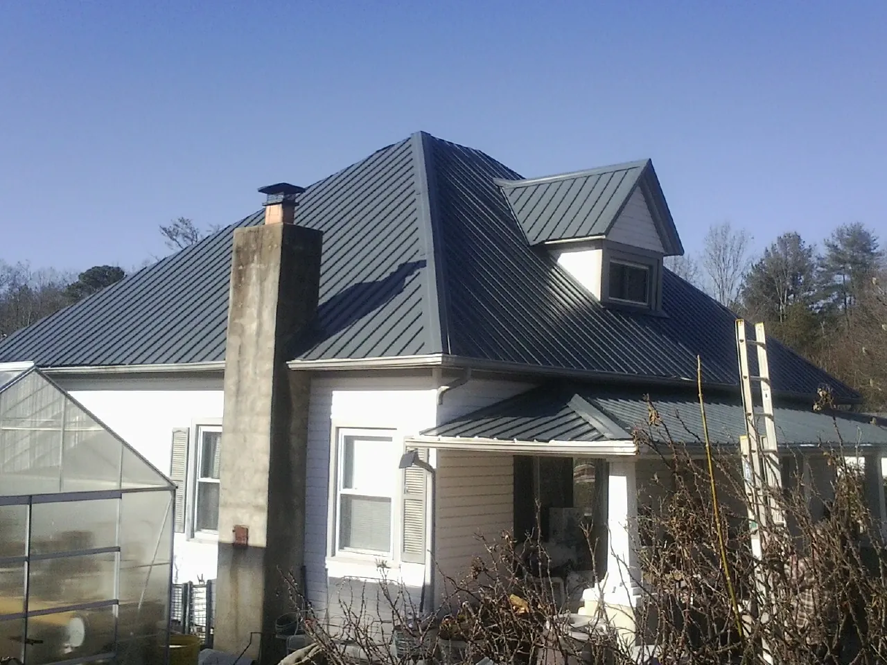 Dark blue standing seam metal roof on a white farmhouse with dormer — Slate & Tile Roof Repair by Roofing Brothers in Bell Gardens