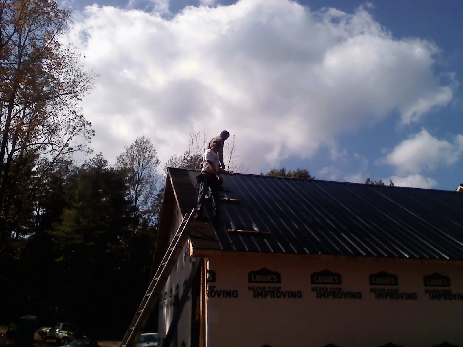 Roofer fastening dark metal panels high against a cloudy sky, from a Roof Inspection job in Bell Gardens